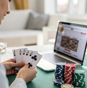 A gambler with playing cards on hand in front of a laptop with casino platform on the screen and chips are piled up on the side